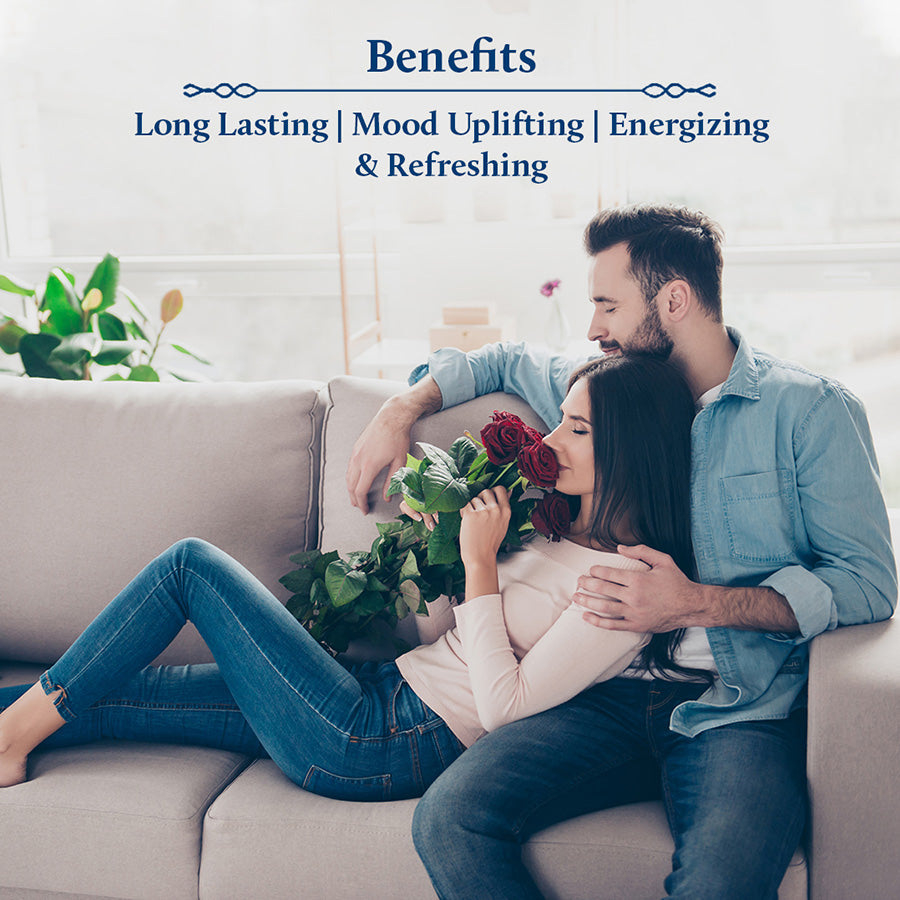 A couple is sitting on the sofa while the girl holds a bouquet of roses and smells them.
